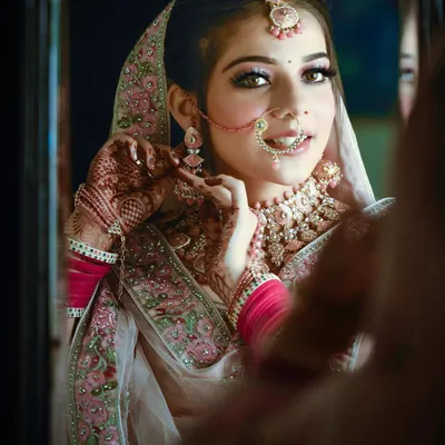 A beautiful getting-ready shot of the bride looking into a mirror. This candid moment captures her adjusting her earring, with a soft smile that reflects her excitement for the day ahead.
