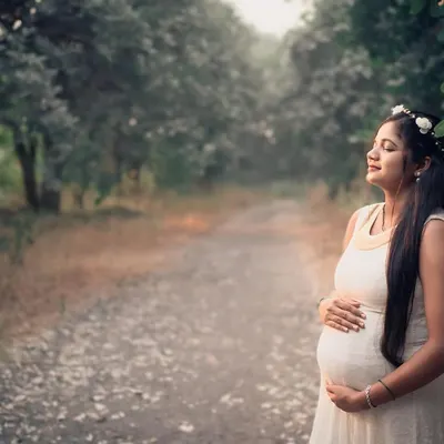 A serene solo portrait of a mother-to-be enjoying a quiet moment on a peaceful forest path. The natural light filtering through the trees creates a soft and gentle atmosphere.