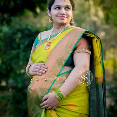 A stunning outdoor portrait of a mom-to-be in a vibrant lime green and gold silk saree. The traditional jewelry and radiant smile complete the look.