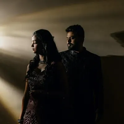 A stunning portrait using projected light to create dramatic rays. The couple stands in the shadows, creating a moody and cinematic feel perfect for an engagement or sangeet shoot.
