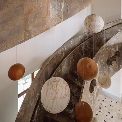 The sculptural staircase at Rehethaan is a celebration of form and material. Clad in dramatic brown marble, it curves its way up, with a celestial installation of spheres hanging in the void.