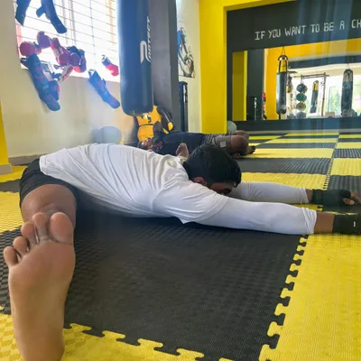 A member performs a deep pancake stretch on the mats, an essential cool-down for improving hip mobility and flexibility.