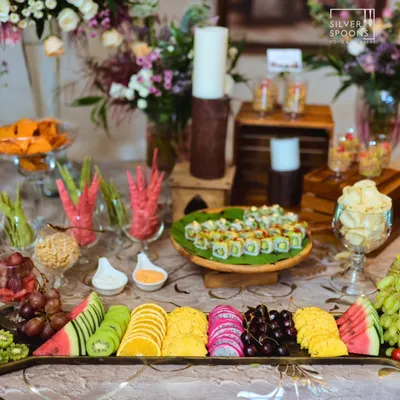 A lavish spread featuring a variety of global and local favorites. The table includes a platter of fresh sushi, an assortment of colorful cut fruits, and other appetizers, perfect for a birthday celebration.