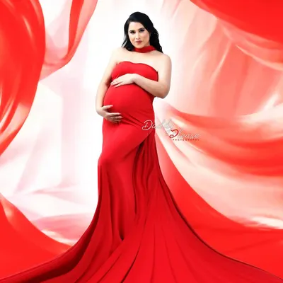 A powerful studio portrait featuring a vibrant red mermaid gown with a dramatic, flowing train. The swirling red fabric in the background creates a sense of movement and high fashion.