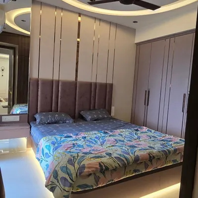 This master bedroom combines layers of texture for a cozy feel. The design features a plush upholstered headboard, elegant gold-tone metal inlays, and a curved false ceiling with concealed lighting.