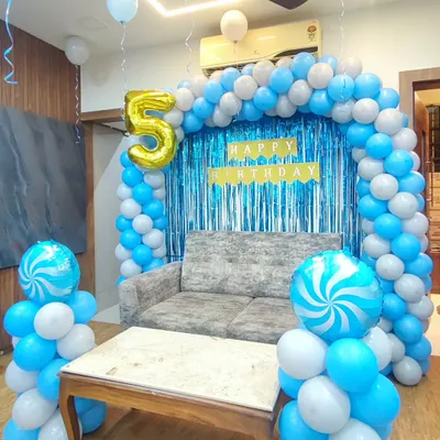 A simple and elegant birthday setup for a fifth birthday using a blue and white color scheme. The decoration features a balloon arch framing a blue shimmer backdrop, with two candy-swirl foil balloons on columns.