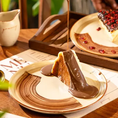 A river of warm chocolate sauce being poured over a San Sebastian cheesecake. This shot is pure indulgence and designed to trigger cravings.