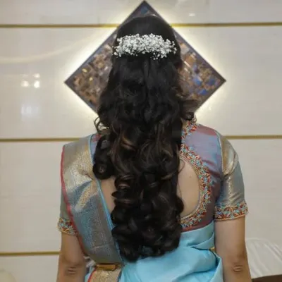 A simple and elegant hairstyle for a reception or party. This look features soft, voluminous curls with the top half pinned back and adorned with a delicate baby's breath hairpiece.