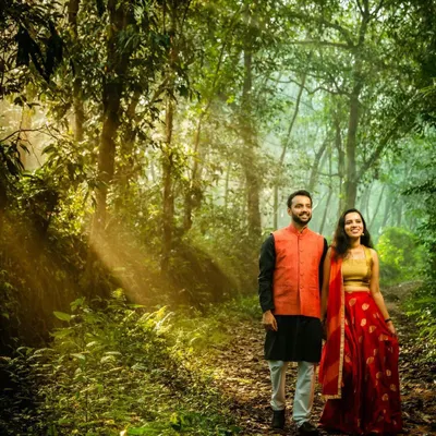 A couple walks through a forest path as beautiful sunbeams filter through the trees. This golden hour photography creates a magical and romantic atmosphere, perfect for an outdoor pre-wedding shoot.