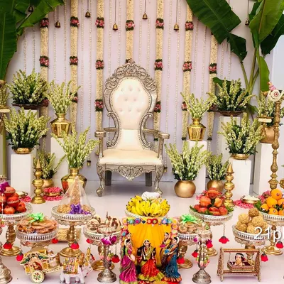An elegant and classic Seemantham setup featuring a silver throne, fresh jasmine and tuberose flower arrangements, and large banana plants for an authentic traditional feel. The foreground is filled with auspicious items and doll displays.