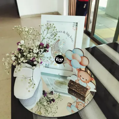 This sweet centerpiece captures the essence of a teddy bear theme. It features a cute bear and balloon cutout, a framed print with a heartfelt quote, and a baby shoe holding delicate flowers, all arranged on a mirrored tray.