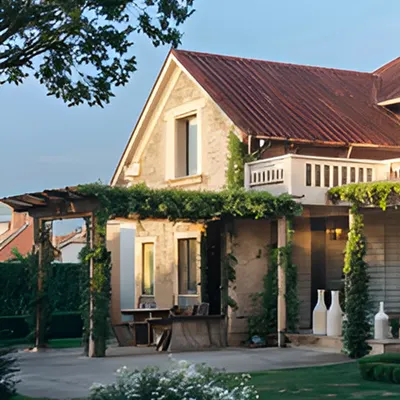A blend of sloping red roofs, a vine-covered pergola, and soft neutral facades brings this home into harmony with its lush green landscape. It is a statement in contemporary architecture rooted in classic forms.