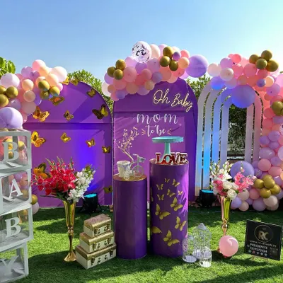 An outdoor rooftop baby shower with a vibrant butterfly theme. This setup features purple arched backdrops, an organic balloon garland in pink and gold, and transparent "BABY" blocks. The "Mom to be" sign and floral arrangements add a personalized touch.