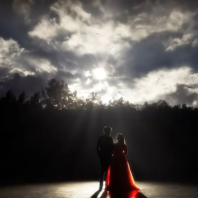 A dramatic silhouette of a couple against a powerful, cloud-filled sky at sunset. This pre-wedding shot uses light and shadow to create a powerful, almost mythical portrait of their love.