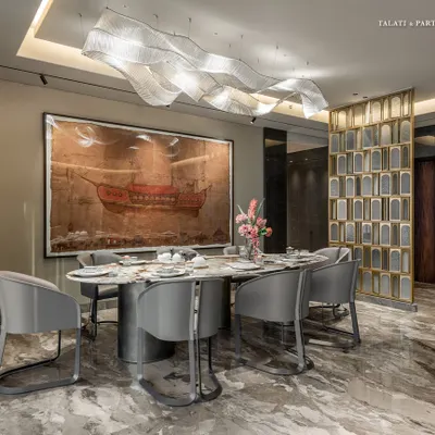 This dining area in a Shivaji Park residence is envisioned as a central anchor of the home. A contemporary theme with a nod to tradition is set by a statement wall etched with ancient Indian texts, while a dramatic wavy light fixture floats above the marble table.