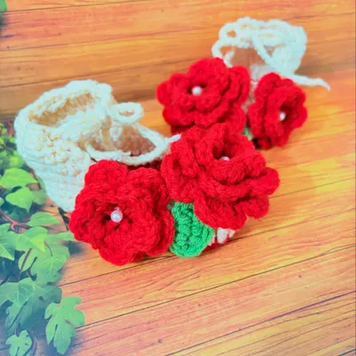 A close-up of my handmade booties with vibrant red flowers. Each flower is centered with a small pearl for a touch of elegance.