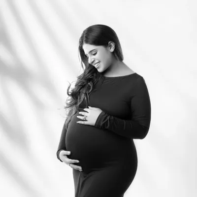 A quiet moment of connection. This beautiful black and white portrait captures a mother-to-be gently cradling her baby bump, her soft smile filled with love. The shadowed lighting adds depth and emotion.