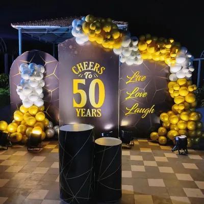 A classy 'Cheers to 50 Years' celebration. This outdoor setup uses a sophisticated black and gold theme with elegant backdrops, a balloon arch, and uplighting for a dramatic effect.