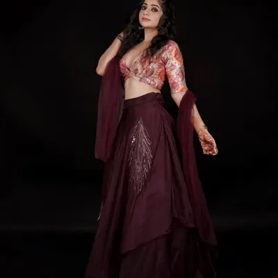 This stylish party-wear lehenga features a floral print crop top and a deep wine-colored asymmetrical skirt. The silver embroidery on the skirt adds a touch of elegance, making it a great rental for a cocktail party or reception.
