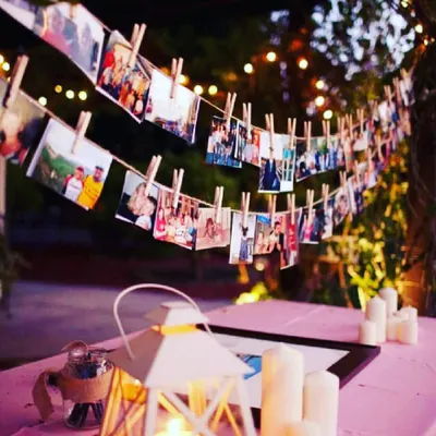 A rustic and charming way to display your memories. I create a photo garland using twine and wooden clothespins, perfect for an outdoor or indoor setting, illuminated by candles and string lights for a warm evening glow.