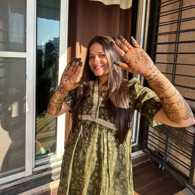 A happy bride basking in the sun, showing off her full bridal mehndi. Her smile says it all, and the natural light beautifully highlights the rich color of the stain.