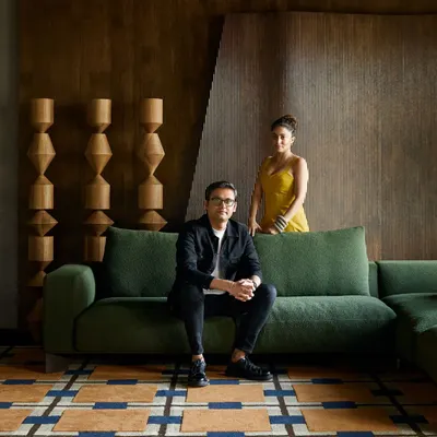 A portrait of us within one of the living room setups at the Ventura gallery. The space is designed with a mix of modern organic furniture, a colorful geometric rug, and warm wood paneling to feel like a real, curated home.