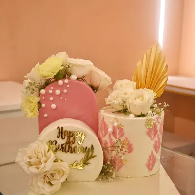 A modern art piece for an 80th birthday. This set includes a fault line cake with pink and pearl details and a stenciled cake, both adorned with fresh white flowers for a truly unique and artistic celebration.