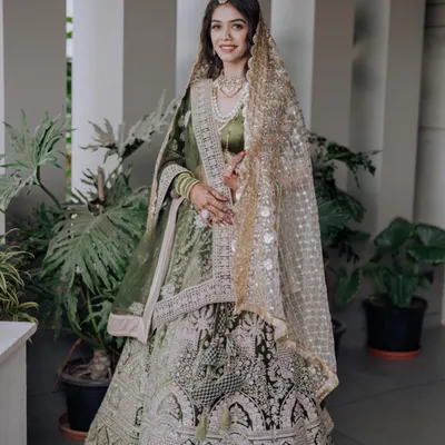 A bride looking radiant in a beautiful olive green lehenga. The intricate silver embroidery and delicate net dupatta create a look of timeless elegance, perfect for a daytime wedding or reception.