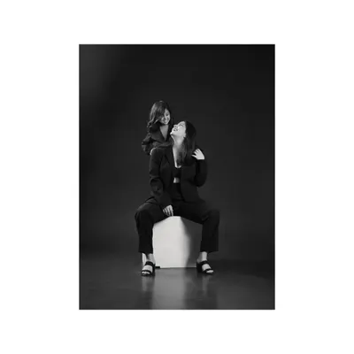 A mother and daughter, dressed in matching black suits, share a laugh against a dark, moody background. This classic black and white style creates a powerful, dramatic portrait of their joyful bond.