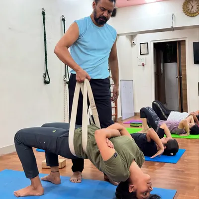 Here, I am providing hands-on assistance with a yoga belt for Grivasana (Neck Pose). This ensures the student maintains proper form, which is crucial for safely strengthening the neck, back, and pelvic floor muscles in this advanced posture.