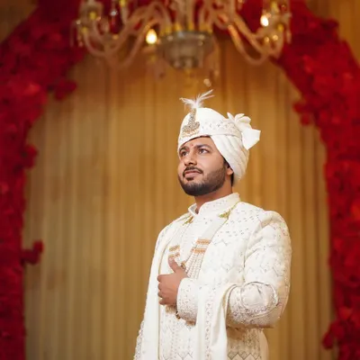 A portrait of the groom, looking sharp and regal in his ivory sherwani. The elegant decor and lighting highlight his sophisticated wedding day look.
