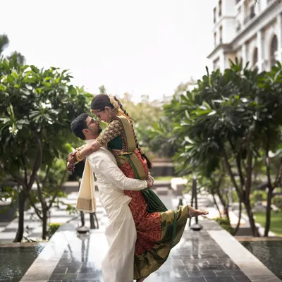 A playful and romantic shot of the couple. The groom lifts his bride, showing the beautiful drape of her traditional red and green Kanjivaram saree against his classic white veshti. It’s a moment of pure happiness.