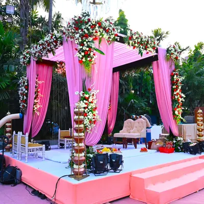A beautiful sundowner wedding mandap at The Acres Club. The pink drapes and heavy floral arrangements with red and white flowers create a romantic and vibrant setting for the ceremony.