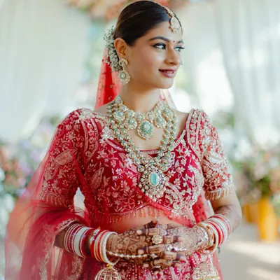 A beautiful portrait of my bride Mansi, looking radiant for her pheras. The look features a classic red lip, defined eyes, and a clean, elegant bun, perfectly complementing her stunning red lehenga and polki jewelry.
