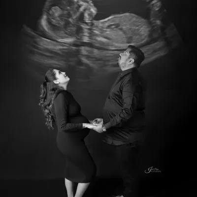 A creative and striking black and white portrait. The couple looks up in awe at their baby's sonogram, which is projected above them, creating a unique and meaningful image.