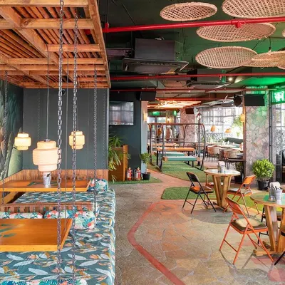 A wide shot of the jungle-themed Social Offline in Gurugram. This photo captures the eclectic mix of seating, including the unique swing chairs and vibrant murals.