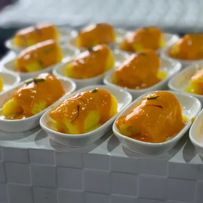 A delicious mango-based dessert served in individual portions. Each dish is topped with a rich, smooth mango sauce and garnished with saffron strands for an elegant finish.