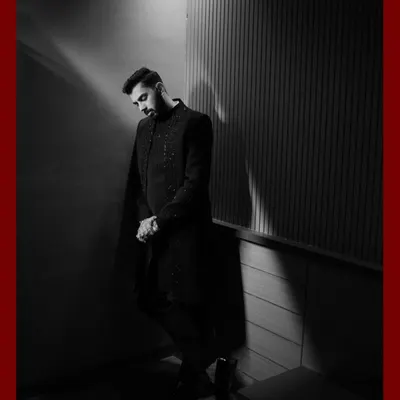 A dramatic black and white portrait of the groom. The strong shadows and focused lighting create a powerful and stylish image, showcasing his sharp attire and confident presence.