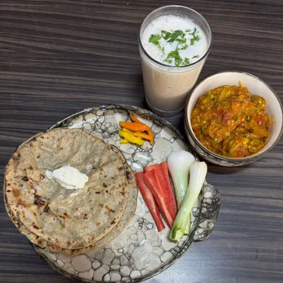 A rustic and hearty winter meal of Bajra Rotlo topped with a dollop of white butter, served with Baigan Bharta, fresh salad, and a glass of chaas. This is traditional comfort food at its best.