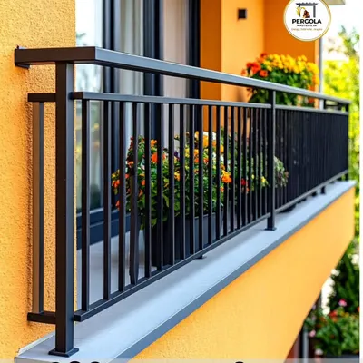 A classic and sturdy black metal railing with vertical balusters installed on a brightly colored balcony. The simple, clean design provides essential safety while complementing the building's cheerful exterior.