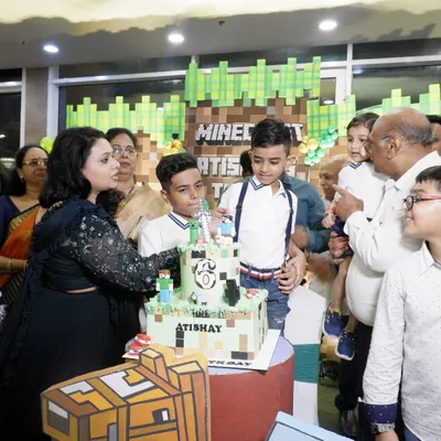 A perfect Minecraft-themed birthday party comes together with a custom cake. Here, the birthday boy, Atishay, is surrounded by family, ready to cut his amazing block-themed cake.