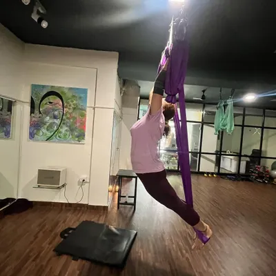 Using the aerial hammock allows for deeper stretches and relieves joint pressure. This image shows a student working on flexibility and strength, supported by the silk.