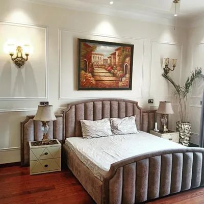 A master bedroom designed with classic elegance. It features a channel-tufted upholstered bed, traditional wall moulding, classic sconces, and rich wooden flooring for a timeless and cozy feel.
