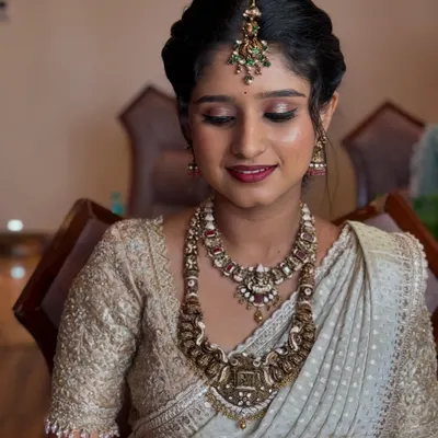 A beautiful makeover for Ramya, the sister of the bride. Her makeup is soft and elegant, designed to complement her stunning antique jewelry and off-white saree.