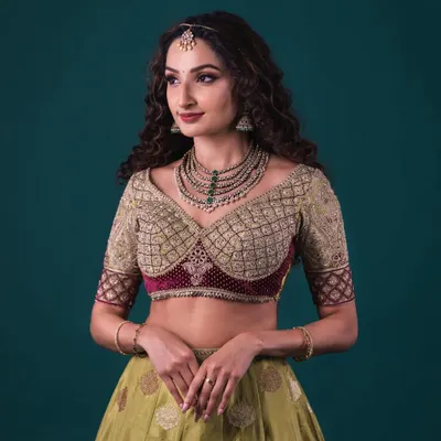 A Banarasi lehenga in olive green, paired with a heavily embroidered blouse. The blouse features a unique sweetheart neckline and a contrasting maroon velvet panel.