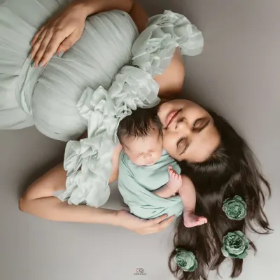 A beautiful overhead portrait of a new mom and her sleeping baby. The soft mint green tones and floral hair accents create a peaceful and artistic image.