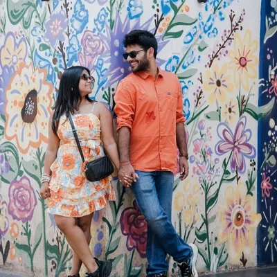 A vibrant and fun pre-wedding shot of a couple posing against a colorful floral mural in Goa, perfectly capturing their playful energy and the lively local art.