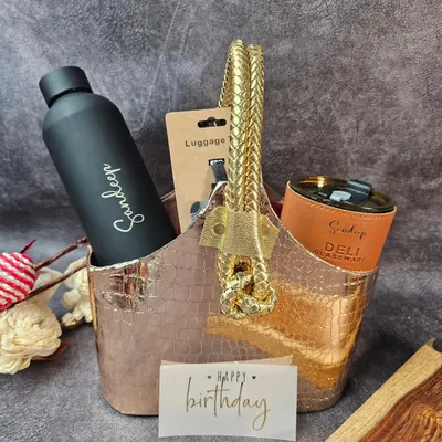 A personalized birthday hamper for your soulmate. This stylish basket includes a custom bottle, a travel mug, and a luggage tag, all in a sleek black and rose gold theme.