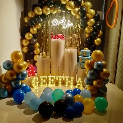 A classic bride-to-be party setup with a black and gold balloon arch and a "Bride to be" neon sign. The name "GEETHA" is spelled out in marquee letters.