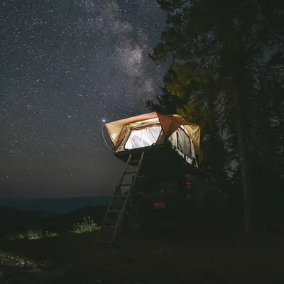 A rooftop tent, elevated for a better view, is illuminated under a breathtaking starry sky. This setup is perfect for those who love to combine road-tripping with a comfortable night of stargazing.